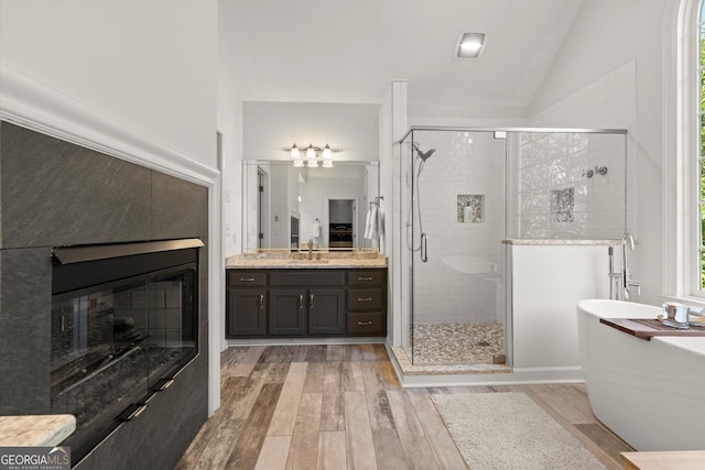 bathroom with wood finished floors, a stall shower, a soaking tub, vanity, and vaulted ceiling