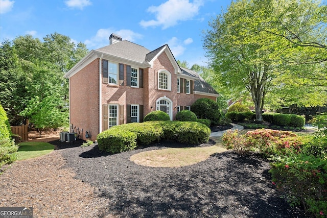 view of front of property with a chimney, brick siding, and central air condition unit