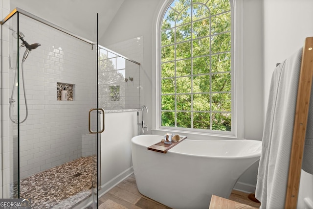 bathroom with a soaking tub, a shower stall, wood finished floors, baseboards, and vaulted ceiling