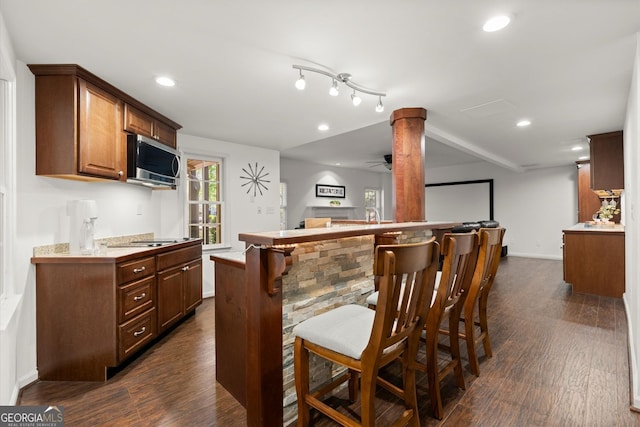 kitchen featuring stainless steel microwave, open floor plan, dark wood-type flooring, a breakfast bar, and light countertops