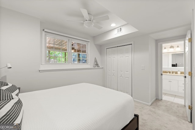 bedroom featuring light carpet, a closet, baseboards, a ceiling fan, and ensuite bath