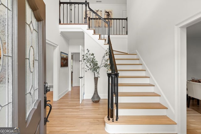 foyer featuring wood finished floors, stairway, a towering ceiling, crown molding, and baseboards