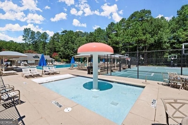 community pool featuring fence, community basketball court, and view of wooded area