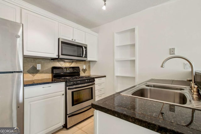kitchen featuring stainless steel appliances, a sink, dark countertops, white cabinetry, and decorative backsplash