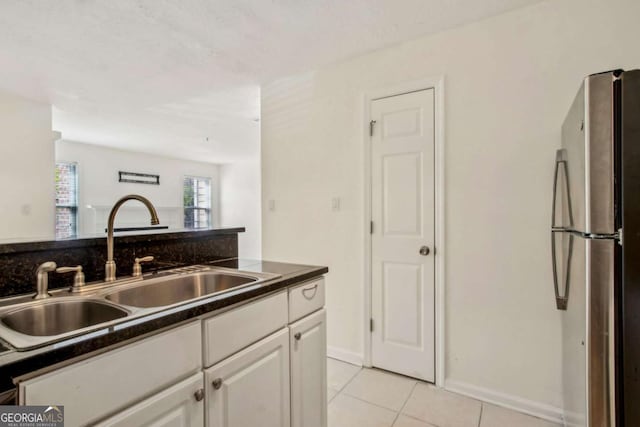 kitchen featuring a sink, dark countertops, freestanding refrigerator, white cabinetry, and light tile patterned floors