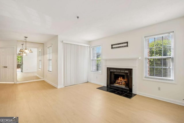 unfurnished living room featuring a fireplace with flush hearth, wood finished floors, baseboards, and an inviting chandelier