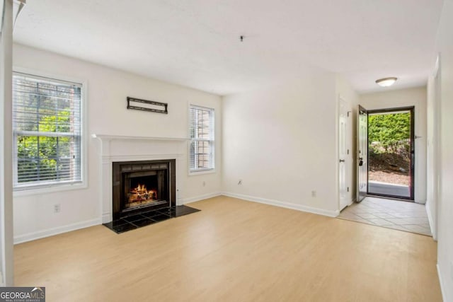 unfurnished living room with a fireplace with flush hearth, wood finished floors, a wealth of natural light, and baseboards