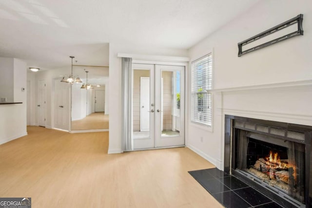 unfurnished living room with a fireplace with flush hearth, wood finished floors, baseboards, and french doors