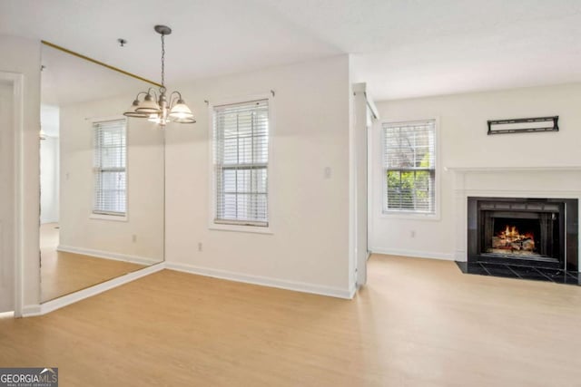 unfurnished dining area with a fireplace with flush hearth, baseboards, wood finished floors, and a notable chandelier