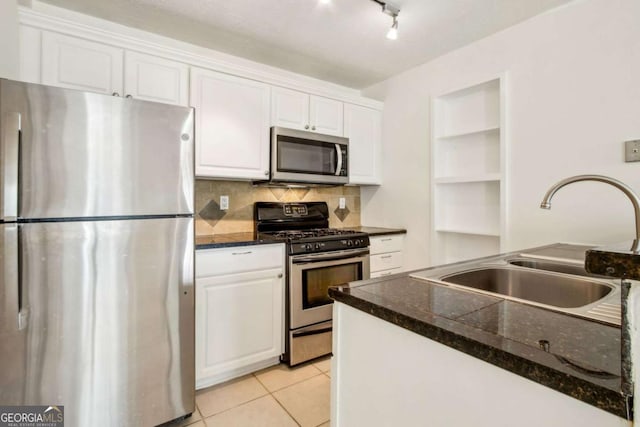 kitchen with dark countertops, a sink, tasteful backsplash, appliances with stainless steel finishes, and white cabinetry