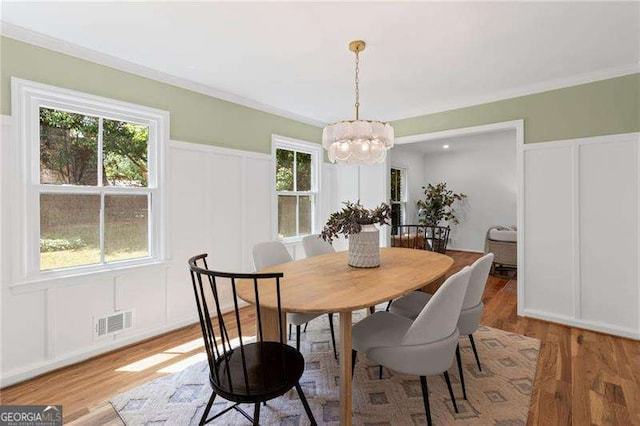 dining area with a notable chandelier, visible vents, a decorative wall, and light wood-style floors