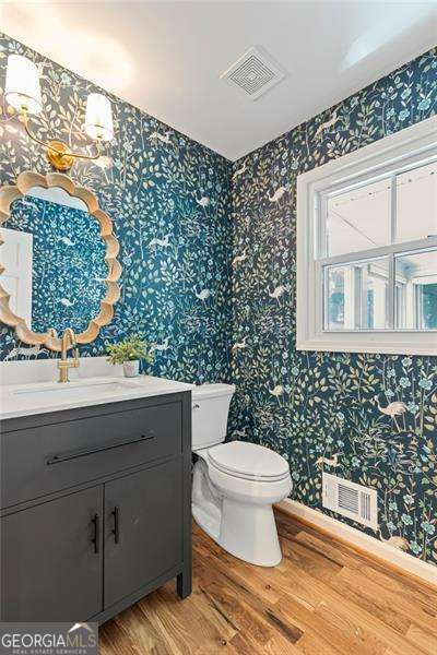 bathroom with wood finished floors, visible vents, toilet, and wallpapered walls