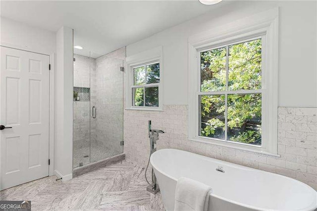bathroom with tile walls, wainscoting, a stall shower, and a soaking tub