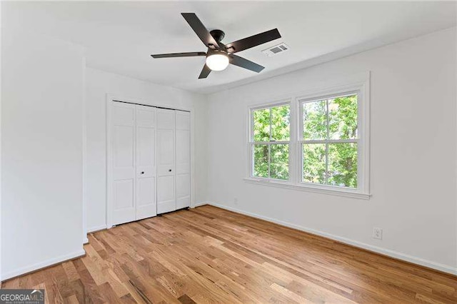 unfurnished bedroom with light wood-style flooring, a closet, baseboards, visible vents, and a ceiling fan