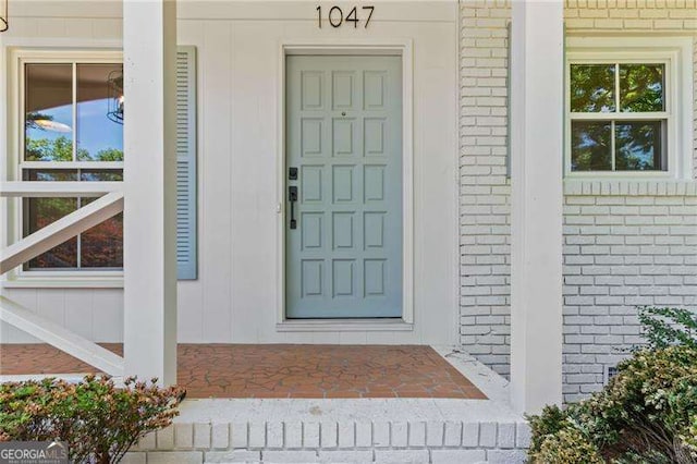 doorway to property featuring a porch and brick siding