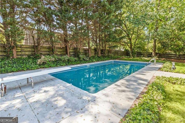 pool with a diving board, a fenced backyard, and a patio area