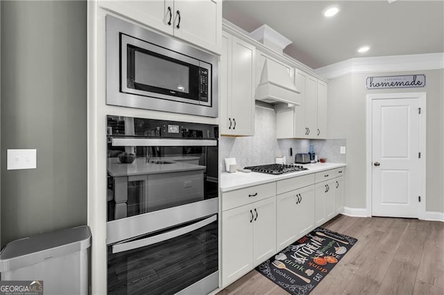 5003 Fairview Cir, Villa Rica, GA 30180 - kitchen with custom exhaust hood, light wood-style floors, white cabinetry, light countertops, and appliances with stainless steel finishes