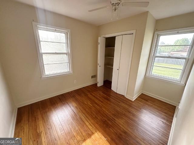unfurnished bedroom featuring baseboards, wood finished floors, a closet, and ceiling fan