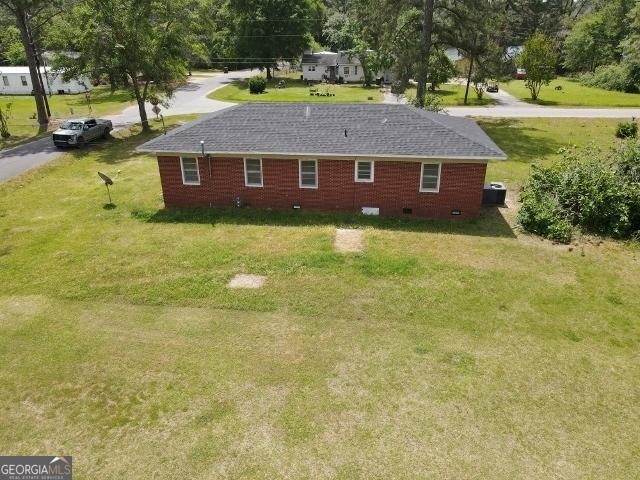 rear view of property with crawl space, a shingled roof, and a yard