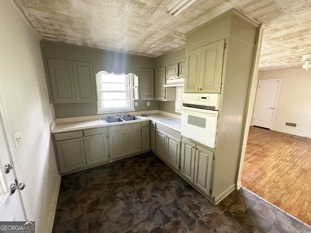 kitchen featuring oven, under cabinet range hood, light countertops, gray cabinets, and a sink