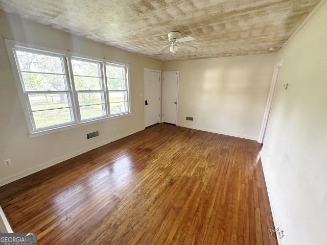 empty room featuring wood finished floors, visible vents, baseboards, and ceiling fan