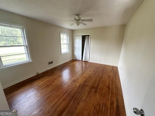 unfurnished bedroom with ceiling fan, baseboards, dark wood-style floors, and a closet