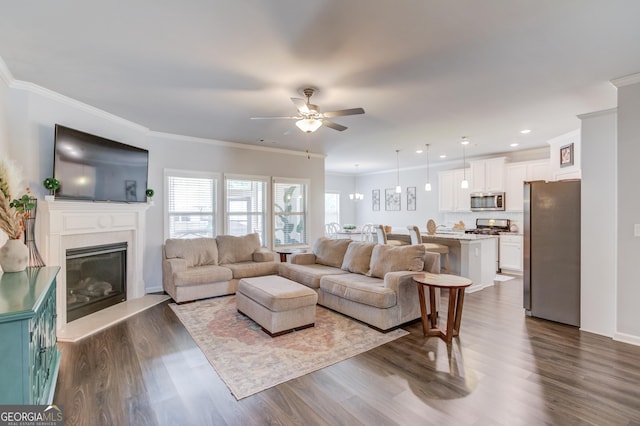 living area featuring ornamental molding, a ceiling fan, dark wood-style flooring, and a fireplace