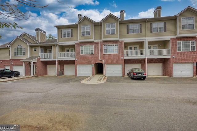 multi unit property featuring a chimney, brick siding, and a garage