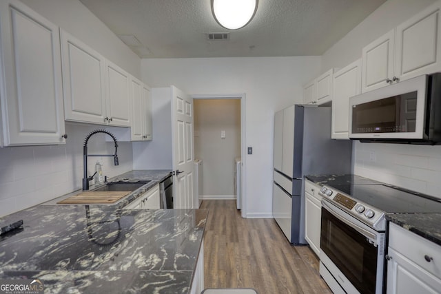kitchen with wood finished floors, visible vents, a sink, tasteful backsplash, and appliances with stainless steel finishes