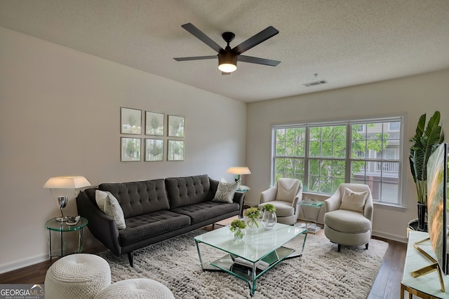 living area featuring dark wood-type flooring, a textured ceiling, visible vents, and a ceiling fan