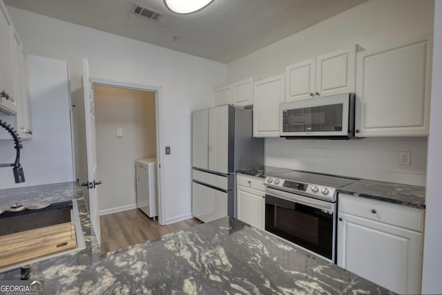 kitchen with white cabinets, washer / dryer, stainless steel appliances, dark wood finished floors, and visible vents