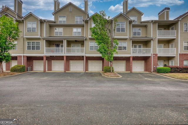 view of front of property featuring driveway, a chimney, brick siding, and central AC unit