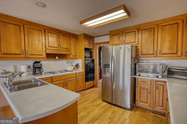 kitchen featuring a warming drawer, black appliances, a sink, and brown cabinetry