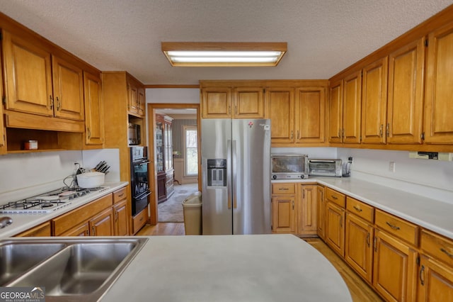 kitchen with black oven, stainless steel fridge, brown cabinetry, and white gas cooktop
