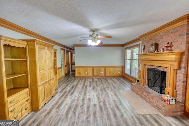 unfurnished living room featuring a textured ceiling, light wood-style floors, crown molding, and a brick fireplace