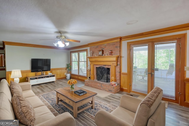 living room featuring a fireplace, crown molding, a ceiling fan, wainscoting, and wood finished floors