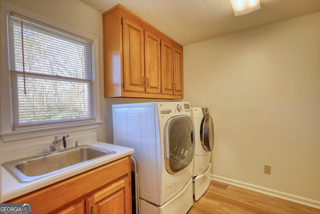 clothes washing area featuring light wood-style floors, a sink, cabinet space, and independent washer and dryer