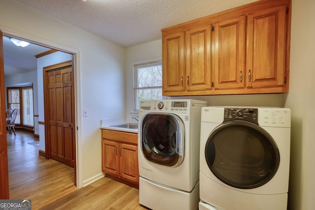 clothes washing area featuring light wood finished floors, a sink, cabinet space, washing machine and dryer, and a textured ceiling