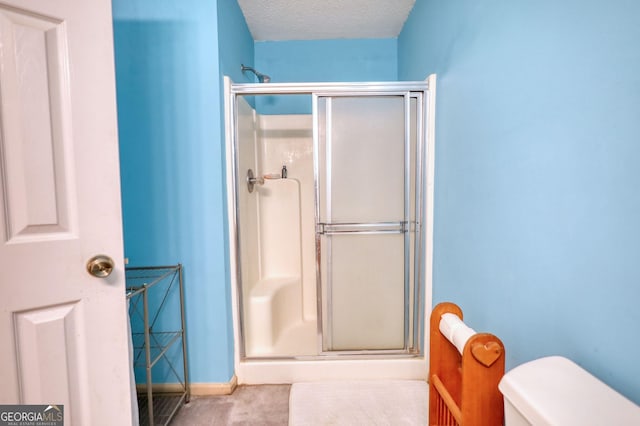bathroom with toilet, a stall shower, a textured ceiling, and baseboards