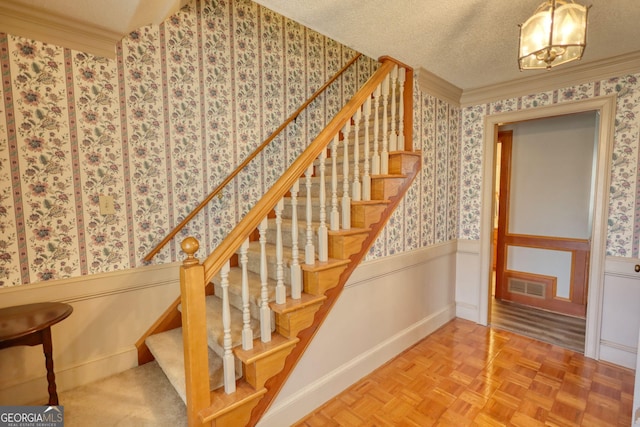 stairs with crown molding, a wainscoted wall, visible vents, and wallpapered walls