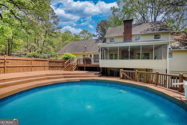 view of swimming pool featuring a deck, fence, a fenced in pool, and a sunroom