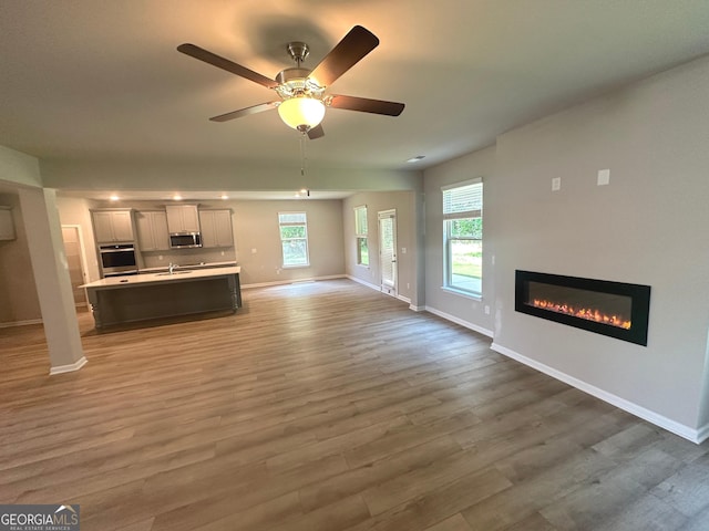 165 Jodi Pl, Locust Grove, GA 30248 - unfurnished living room with baseboards, a glass covered fireplace, light wood finished floors, and plenty of natural light