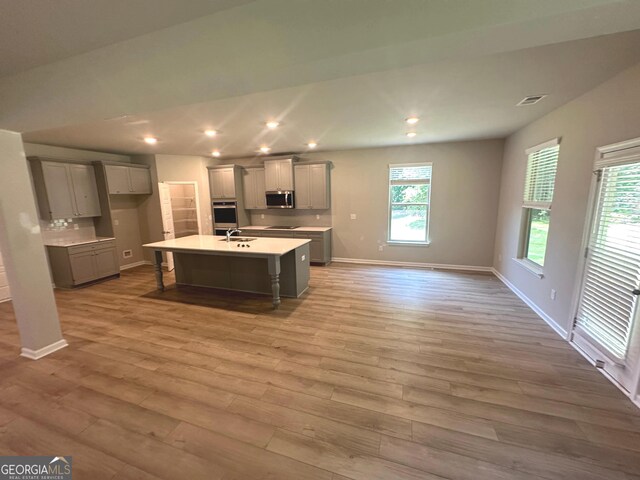 165 Jodi Pl, Locust Grove, GA 30248 - kitchen with stainless steel microwave, a center island with sink, light wood-type flooring, baseboards, and gray cabinets