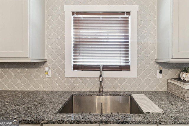 details featuring a sink, dark stone countertops, and tasteful backsplash