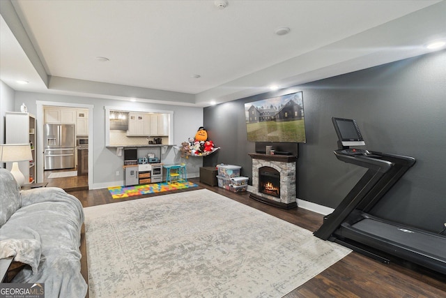 living room with recessed lighting, a tray ceiling, wood finished floors, baseboards, and a fireplace