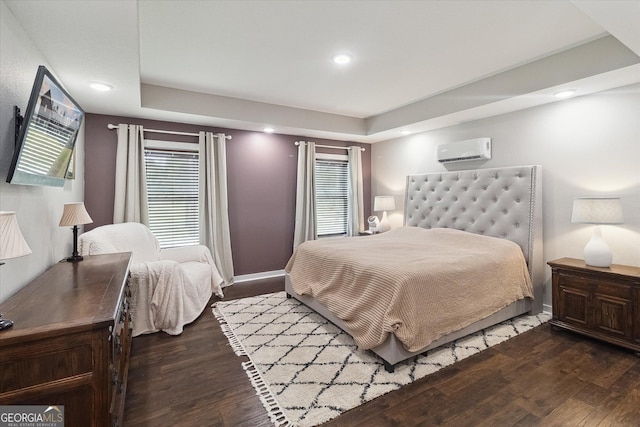 bedroom featuring multiple windows, wood finished floors, a raised ceiling, and a wall mounted air conditioner