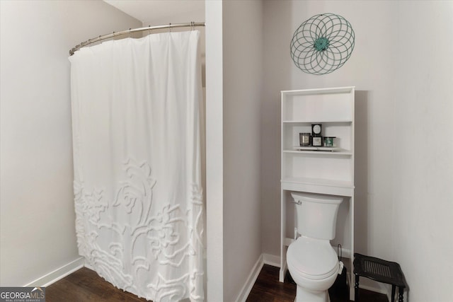 bathroom featuring baseboards, wood finished floors, curtained shower, and toilet