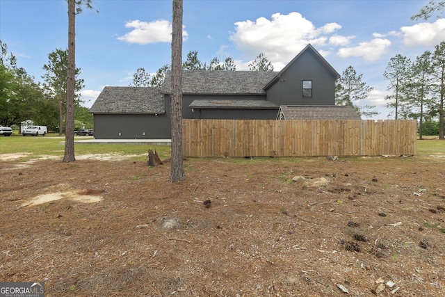 view of side of home with fence and roof with shingles
