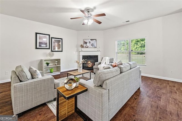 living area featuring a glass covered fireplace, ceiling fan, baseboards, dark wood-style flooring, and visible vents