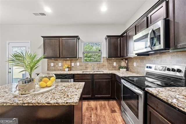 kitchen with a sink, light wood-style floors, dark brown cabinetry, appliances with stainless steel finishes, and visible vents